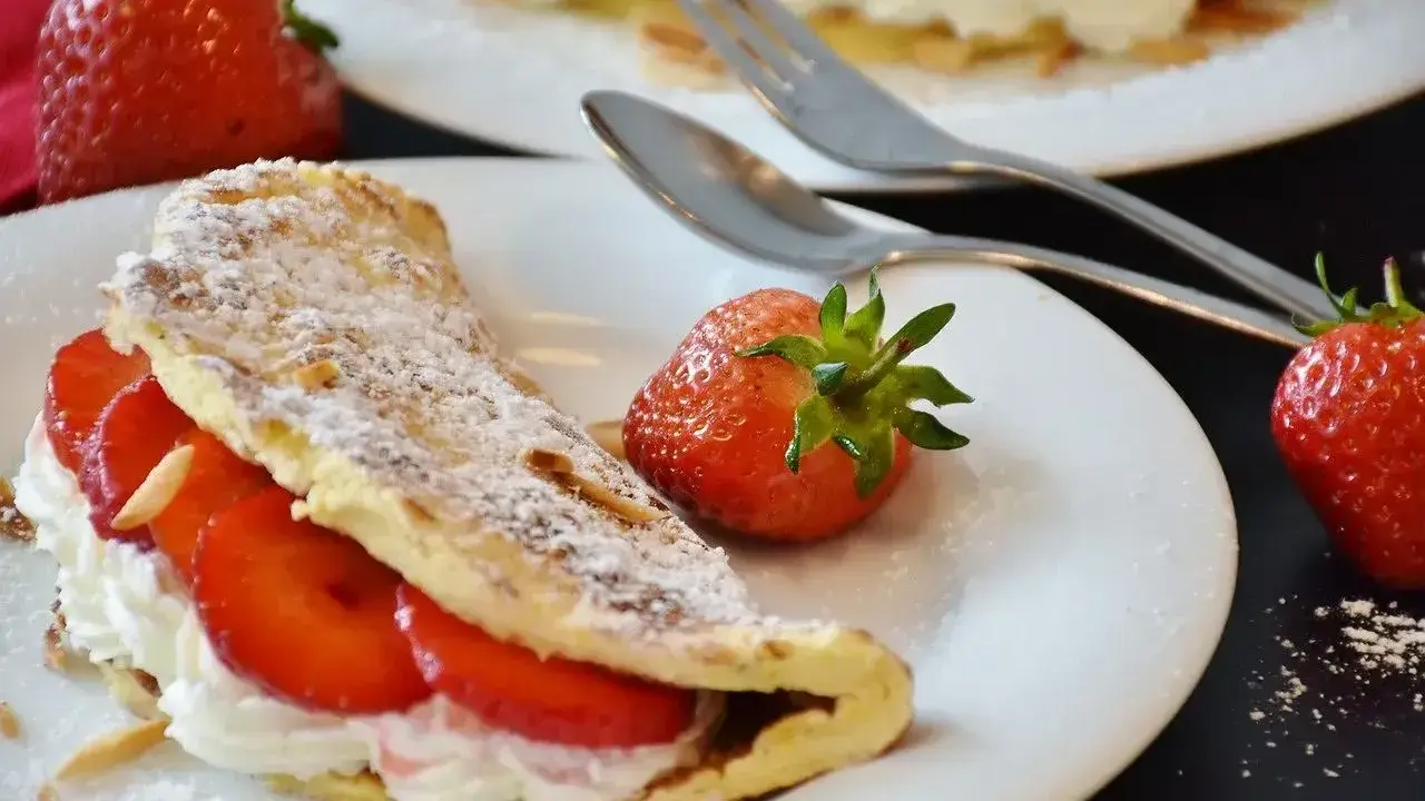 Pyszny omlet z owocami, udekorowany cukrem pudrem i migdałami, z dodatkiem świeżych truskawek.