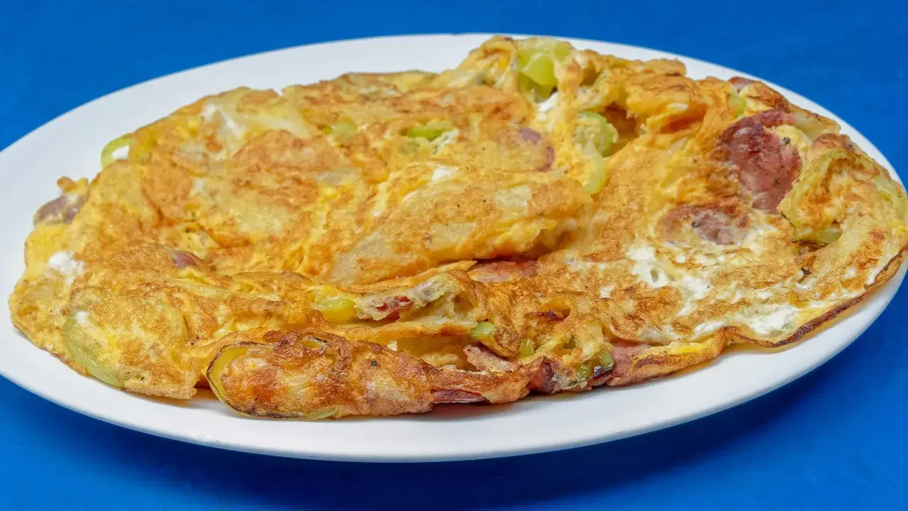 Złocisty omlet na słono z kawałkami kiełbasy i zielonych warzyw, podany na białym talerzu.