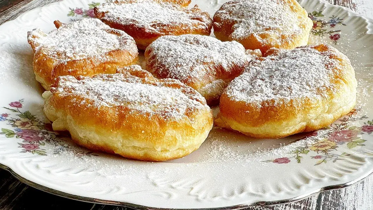 Puszyste racuchy na jogurcie, posypane cukrem pudrem, kuszą swoim złotym kolorem i delikatnością.