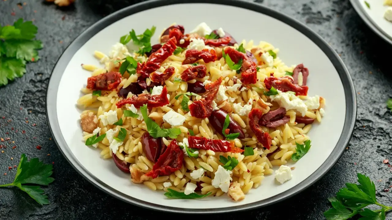 Pyszna sałatka z makaronem orzo, z suszonymi pomidorami, fetą, oliwkami i natką pietruszki.