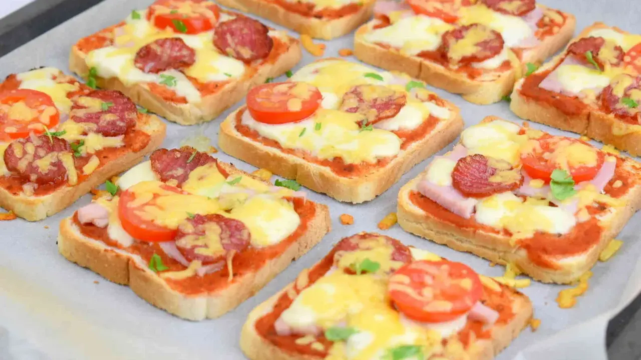 Pyszne, domowe pizza z chleba tostowego z serem, pomidorami i kiełbasą, gotowa do pieczenia.