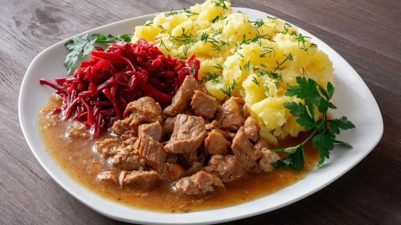 Gulasz z łopatki, ziemniaki z koperkiem i surówka z buraczków na białym talerzu.