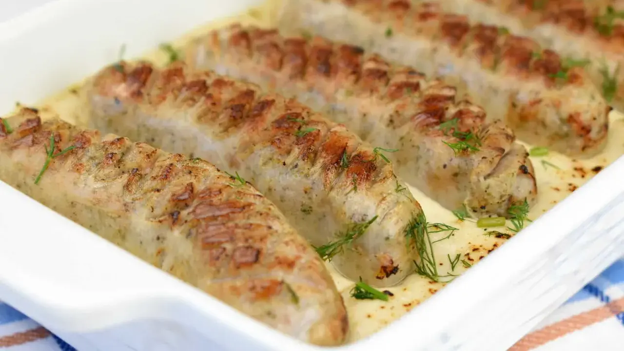 Biała kiełbasa w sosie chrzanowym, zapieczona w naczyniu, ozdobiona koperkiem. Pyszne danie gotowe do podania.