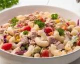 Pyszna sałatka z tuńczykiem, makaronem, pomidorkami, groszkiem i czerwoną cebulą, udekorowana natką pietruszki.