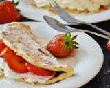Pyszny omlet z owocami, udekorowany cukrem pudrem i migdałami, z dodatkiem świeżych truskawek.