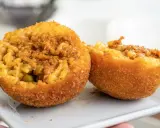 Dwa złociste arancini, przekrojone na pół, ukazują ryż z mięsem i groszkiem. To właśnie arancini co to za przysmak!