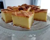 Pyszny sernik na kruchym spodzie, pokrojony na kwadratowe kawałki, prezentuje się apetycznie na szklanej paterze.