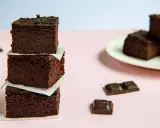 Ciemne, wilgotne brownie z fasoli ułożone w wieżę, obok kawałki czekolady i talerz z kolejnymi ciastkami.