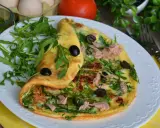 Pyszny omlet z tuńczykiem, rukolą i oliwkami, podany na białym talerzu z żółtym obrusem.