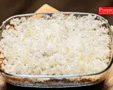 Zapiekanka z ryżem i jabłkami w szklanym naczyniu, gotowa do pieczenia.