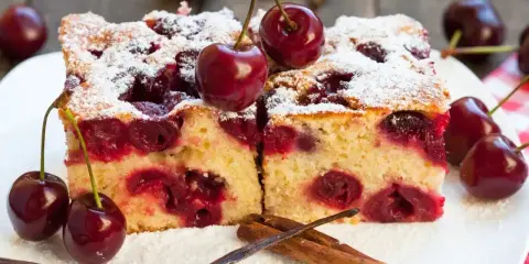 Pyszne ciasto z czereśniami, posypane cukrem pudrem, z dodatkiem lasek wanilii i cynamonu. Idealne na letnie popołudnie.