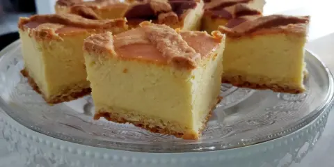 Pyszny sernik na kruchym spodzie, pokrojony na kwadratowe kawałki, prezentuje się apetycznie na szklanej paterze.