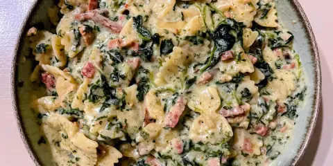 Pyszny makaron farfalle ze szpinakiem i kawałkami boczku w kremowym sosie.