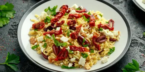 Pyszna sałatka z makaronem orzo, z suszonymi pomidorami, fetą, oliwkami i natką pietruszki.