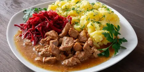 Gulasz z łopatki, ziemniaki z koperkiem i surówka z buraczków na białym talerzu.