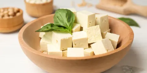Kostki tofu w drewnianej misce z bazylią. Czy tofu można jeść na surowo? Tak, to świetna baza do sałatek i przekąsek.
