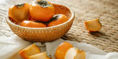 Kaki w koszyku i na obrusie. Czy kaki można jeść ze skórką? Tak, skórka jest jadalna i smaczna.
