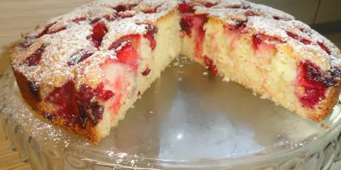 Pyszne ciasto z owocami, posypane cukrem pudrem, prezentuje się apetycznie na szklanej paterze.