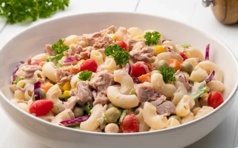 Pyszna sałatka z tuńczykiem, makaronem, pomidorkami, groszkiem i czerwoną cebulą, udekorowana natką pietruszki.