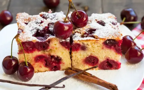 Pyszne ciasto z czereśniami, posypane cukrem pudrem, z dodatkiem lasek wanilii i cynamonu. Idealne na letnie popołudnie.