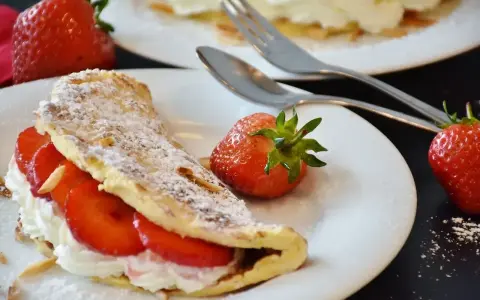 Pyszny omlet z owocami, udekorowany cukrem pudrem i migdałami, z dodatkiem świeżych truskawek.