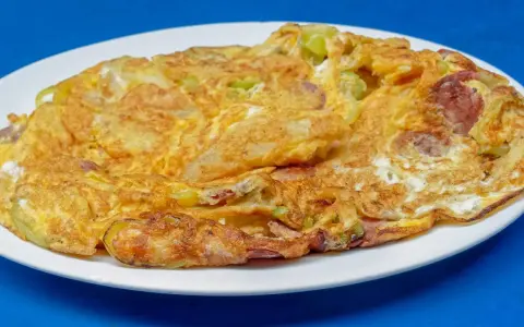 Złocisty omlet na słono z kawałkami kiełbasy i zielonych warzyw, podany na białym talerzu.