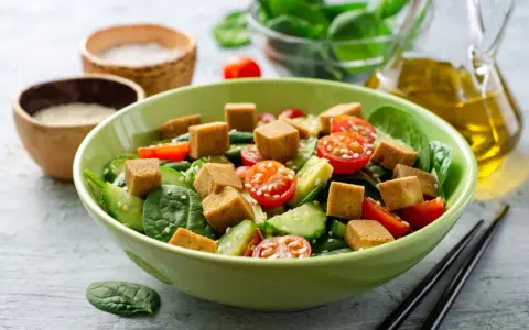 Pyszna sałatka z chrupiącym tofu, pomidorkami koktajlowymi i ogórkiem na świeżym szpinaku. Idealna na lekki posiłek.