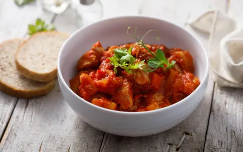 Aromaticzny indyk w sosie curry, podany w białej misce, z dodatkiem świeżych ziół i kromek chleba.