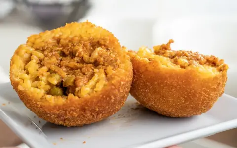 Dwa złociste arancini, przekrojone na pół, ukazują ryż z mięsem i groszkiem. To właśnie arancini co to za przysmak!
