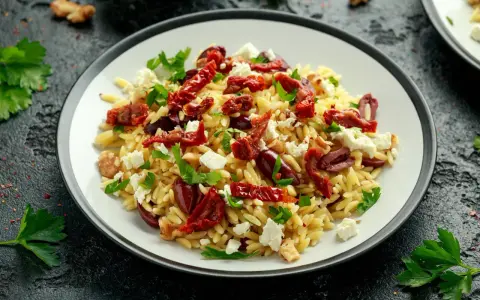 Pyszna sałatka z makaronem orzo, z suszonymi pomidorami, fetą, oliwkami i natką pietruszki.