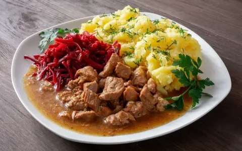 Gulasz z łopatki, ziemniaki z koperkiem i surówka z buraczków na białym talerzu.