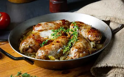Pieczona biała kiełbasa surowa z cebulą i tymiankiem w metalowej patelni.