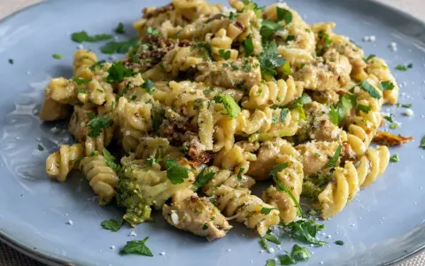 Pyszny makaron z kurczakiem, brokułami i suszonymi pomidorami, posypany parmezanem i natką pietruszki.