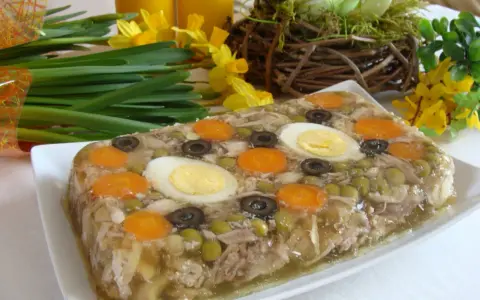 Pyszne nóżki w galarecie z marchewką, jajkiem i oliwkami, ozdobione wiosennymi kwiatami.