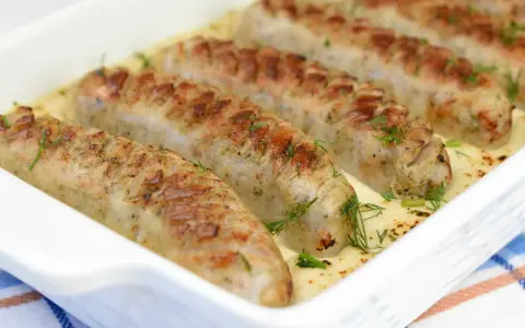 Biała kiełbasa w sosie chrzanowym, zapieczona w naczyniu, ozdobiona koperkiem. Pyszne danie gotowe do podania.