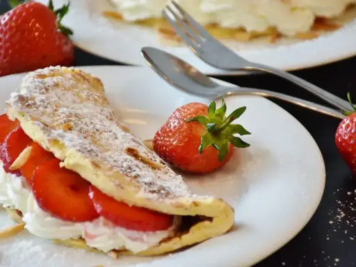 Pyszny omlet z owocami, udekorowany cukrem pudrem i migdałami, z dodatkiem świeżych truskawek.