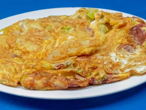 Złocisty omlet na słono z kawałkami kiełbasy i zielonych warzyw, podany na białym talerzu.