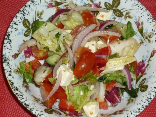 Kolorowa sałatka z mix sałat, pomidorów, ogórka, sera feta i czerwonej cebuli, podana na talerzu z kwiatowym wzorem.