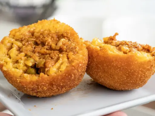 Dwa złociste arancini, przekrojone na pół, ukazują ryż z mięsem i groszkiem. To właśnie arancini co to za przysmak!