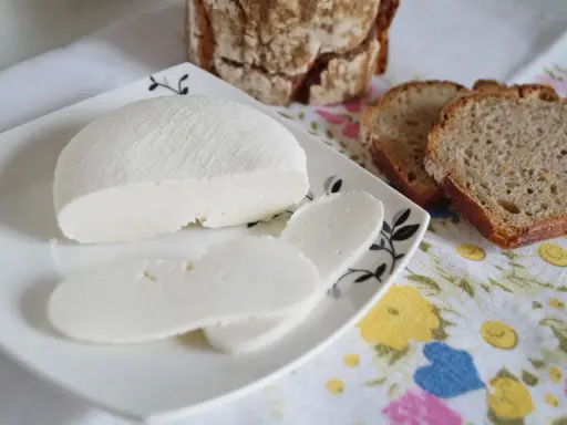 Domowy ser z mleka, pokrojony w plastry, na talerzyku z chlebem. Idealny na śniadanie.