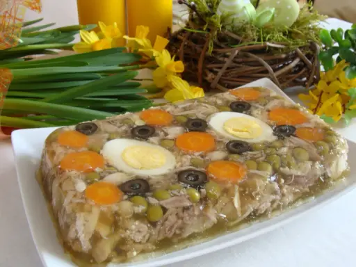 Pyszne nóżki w galarecie z marchewką, jajkiem i oliwkami, ozdobione wiosennymi kwiatami.