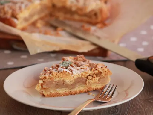 Pyszna tarta z jabłkami, posypana cukrem pudrem i listkiem mięty, czeka na widelcu.