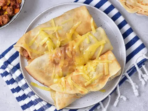 Naleśniki po meksykańsku, zapieczone z serem, obok miseczki z farszem mięsnym i kukurydzą.