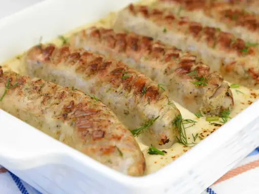 Biała kiełbasa w sosie chrzanowym, zapieczona w naczyniu, ozdobiona koperkiem. Pyszne danie gotowe do podania.