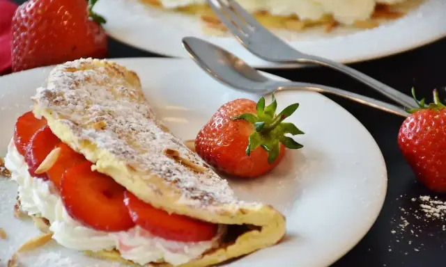 Pyszny omlet z owocami, udekorowany cukrem pudrem i migdałami, z dodatkiem świeżych truskawek.