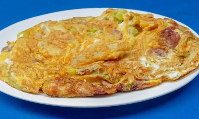 Złocisty omlet na słono z kawałkami kiełbasy i zielonych warzyw, podany na białym talerzu.