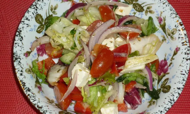 Kolorowa sałatka z mix sałat, pomidorów, ogórka, sera feta i czerwonej cebuli, podana na talerzu z kwiatowym wzorem.