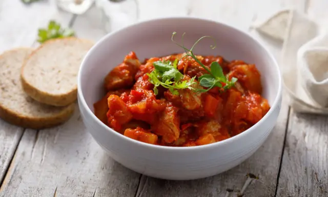Aromaticzny indyk w sosie curry, podany w białej misce, z dodatkiem świeżych ziół i kromek chleba.