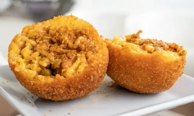 Dwa złociste arancini, przekrojone na pół, ukazują ryż z mięsem i groszkiem. To właśnie arancini co to za przysmak!