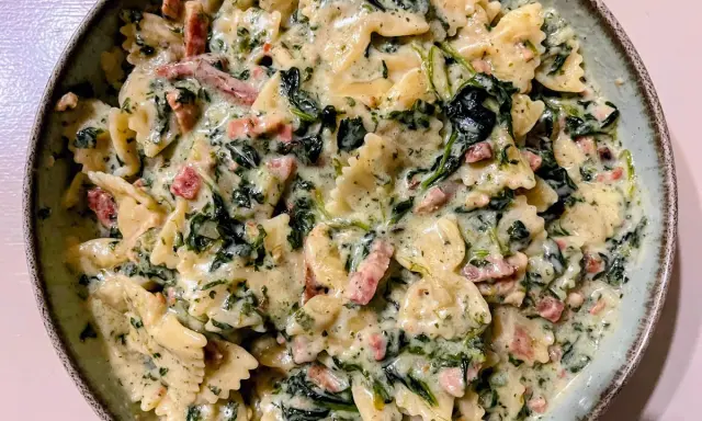 Pyszny makaron farfalle ze szpinakiem i kawałkami boczku w kremowym sosie.